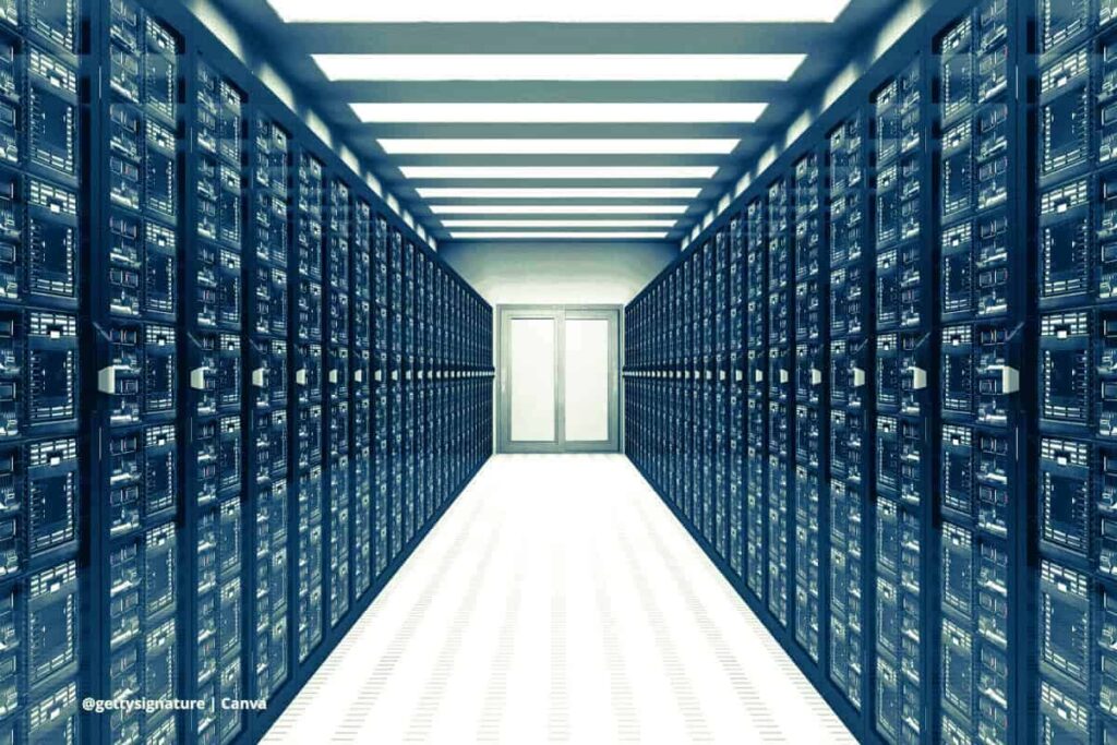 Vista interior de un centro de datos con racks de servidores, infraestructura clave para servicios en la nube y almacenamiento digital. ©gettysignature | Canva Centro de datos con pasillo de servidores iluminados