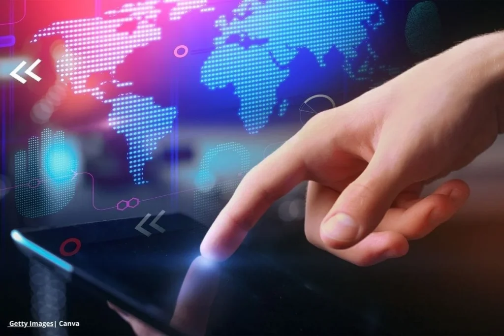 innovación social digital Colombia – mano interactuando con tableta frente a mapa digital del mundo